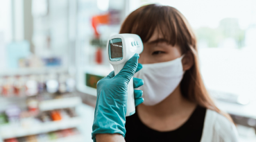 Woman wearing a mask and having temperature checked with a thermometer.